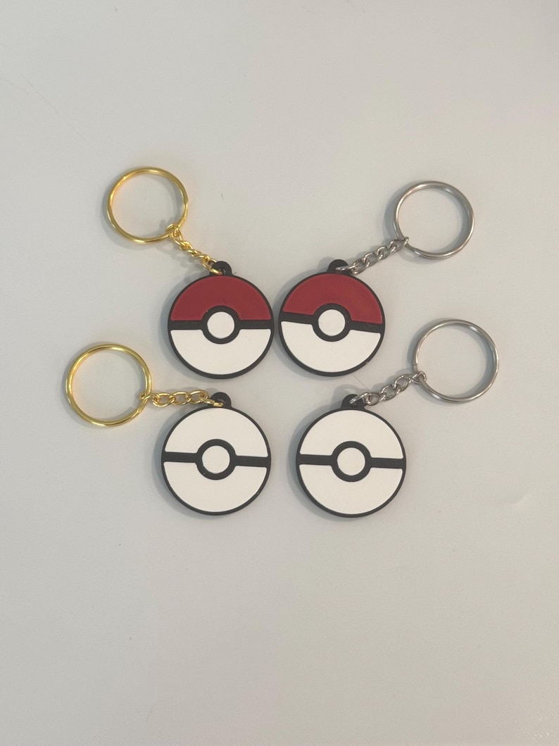 Four Pokéball NFC keychains in red-and-white and black-and-white designs, with gold and silver rings.