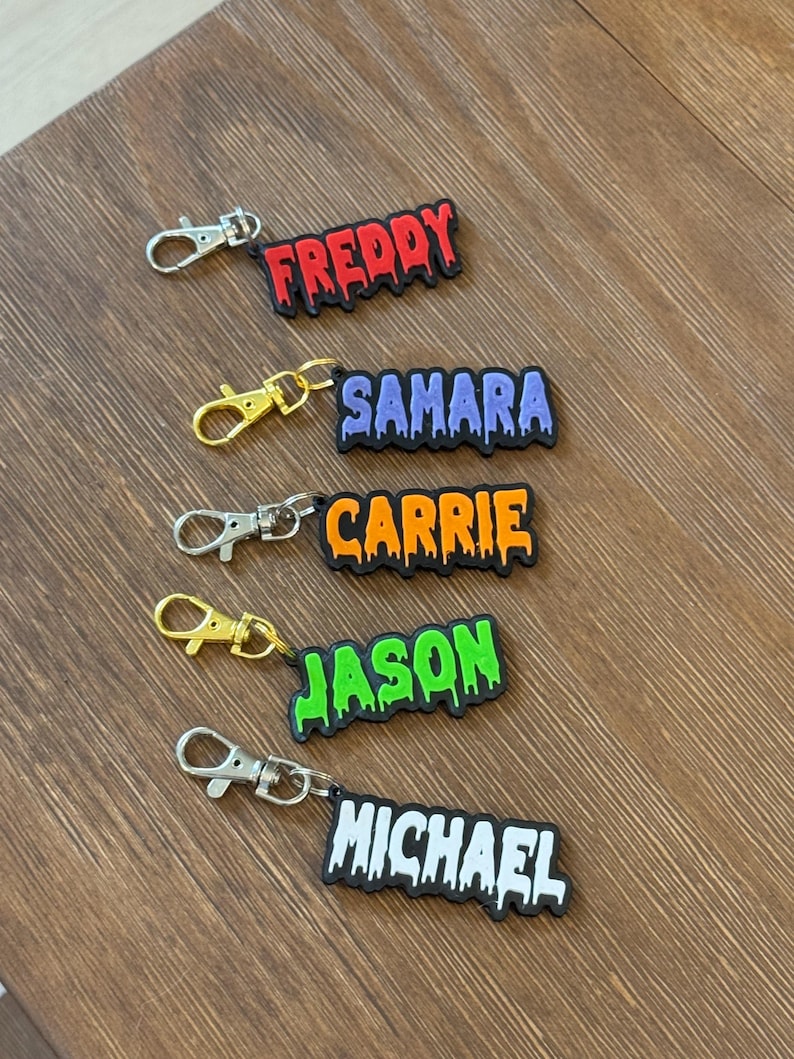 Five personalized spooky font keychains in red, purple, orange, green, and white with metal clasps.